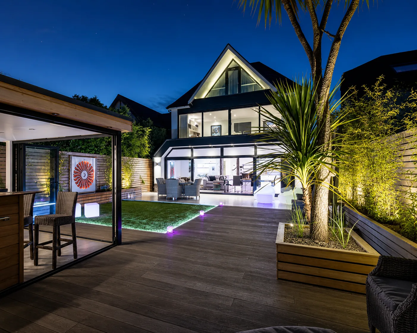 Rear garden and pool terrace lit at night, completed by Morgan Design & Construction at Skyfall House, Poole